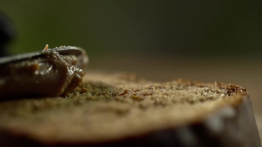 A knife spreads a dark substance over the top of a piece of bread