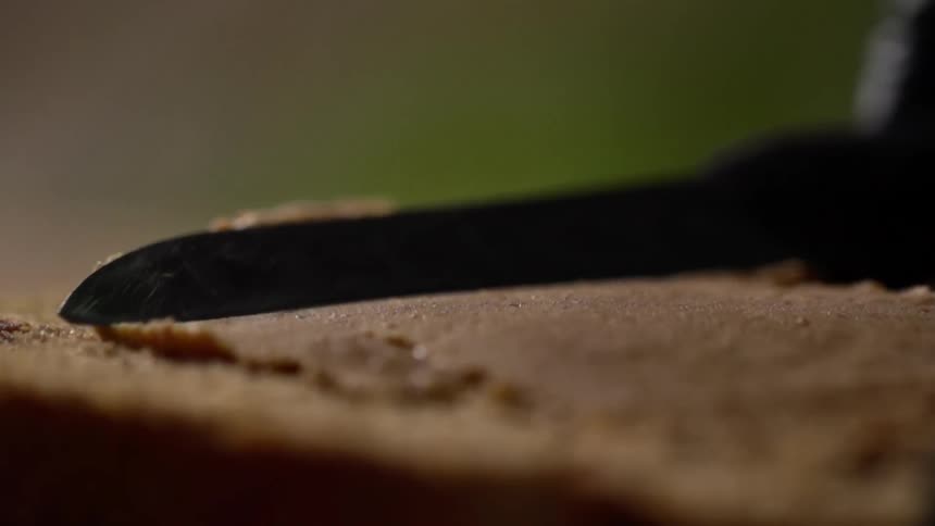 A knife spreads peanut butter on a piece of bread