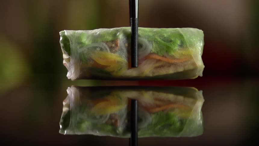 An egg roll is being placed with chop sticks