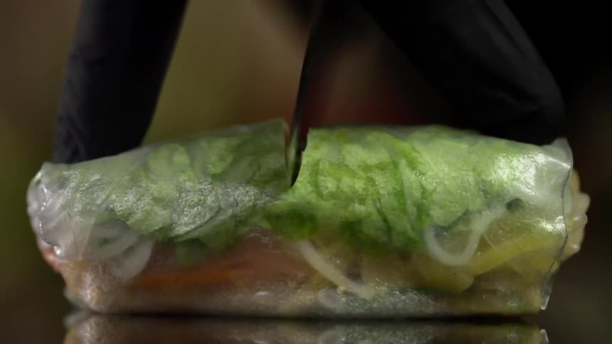 A person slowly cuts through a vietnamese spring roll using a sharp knife