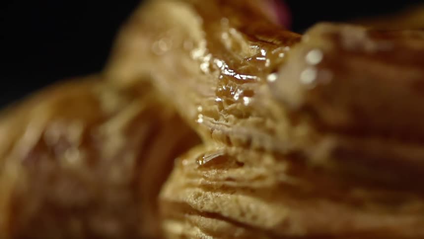 A flaky bread pastry is covered in a small drizzle of honey
