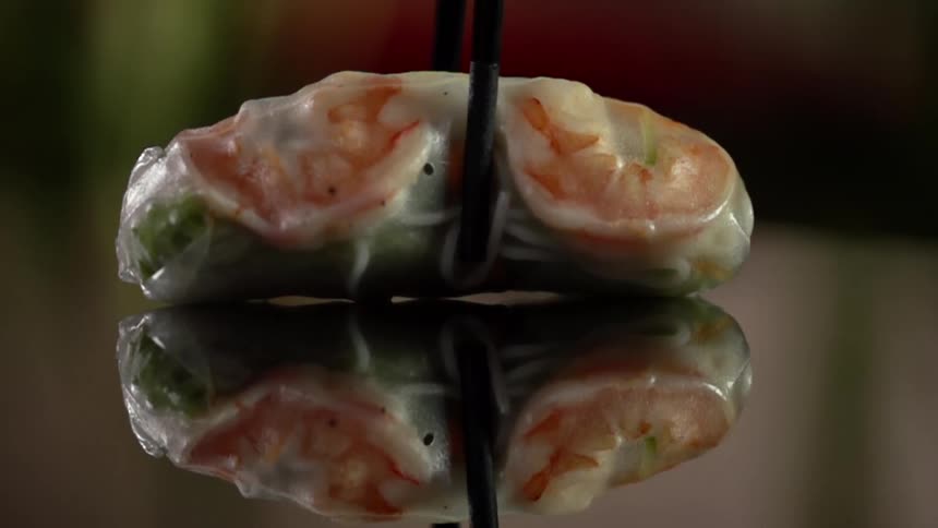 A spring roll held with chopsticks is set on a table