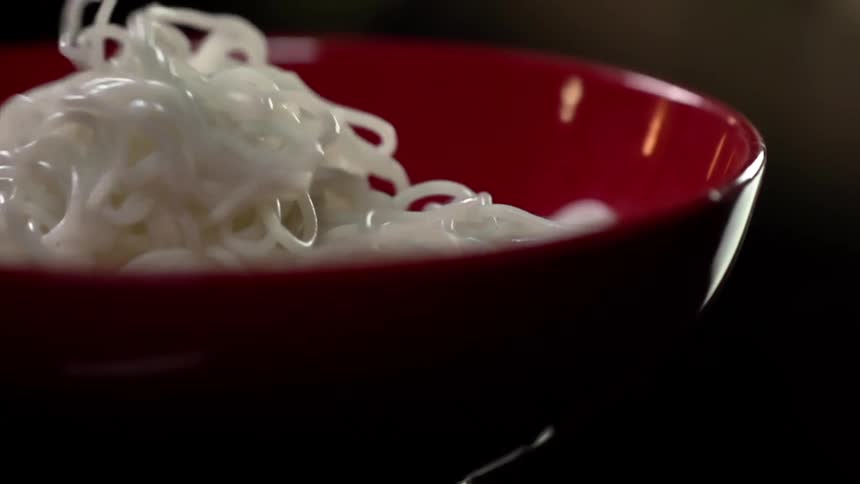 White cooked noodles being served in a red ceramic bowl