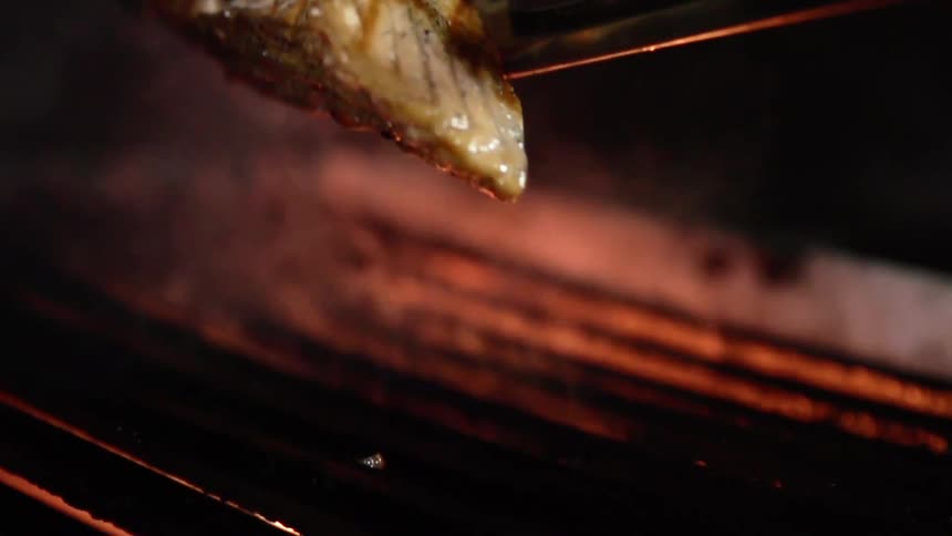 A salmon filet is removed with tongs from a smoking hot grill