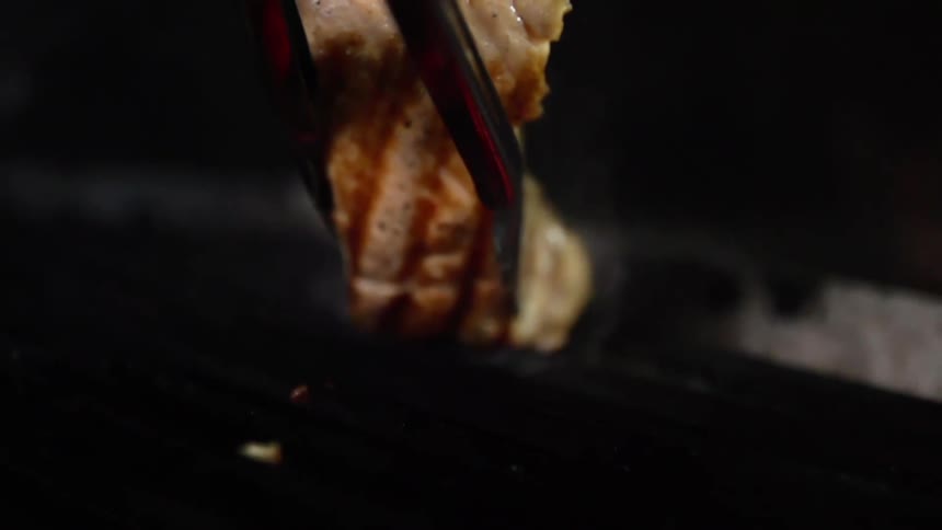 Tongs place fish steak onto smoking grill