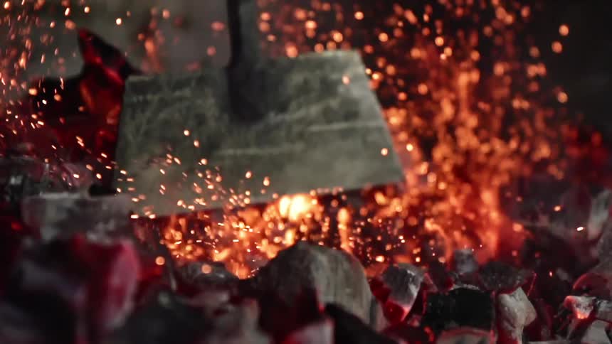 A metal tool stirs heated embers to stoke a flame