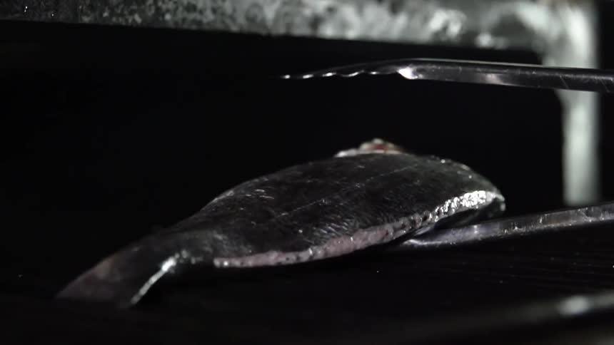 A whole fish is placed on the grate of a grill using tongs