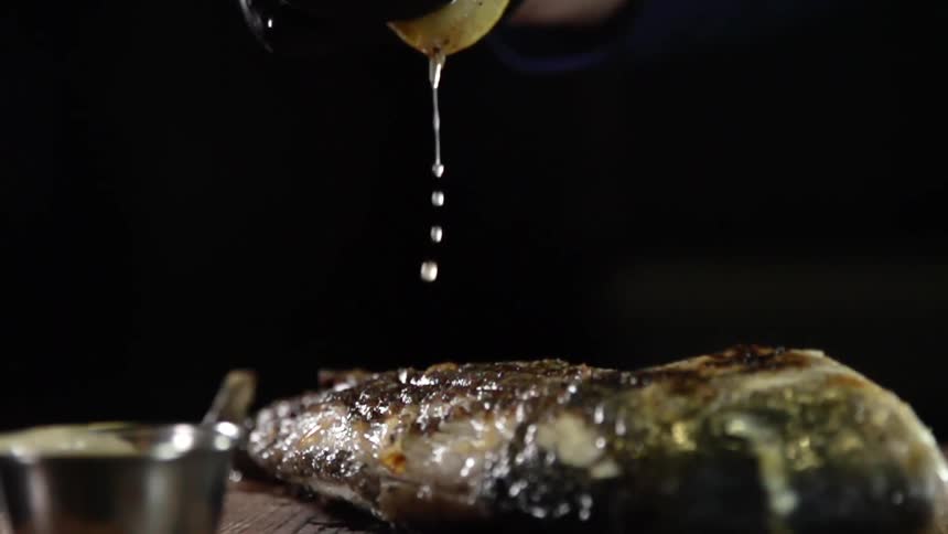 Lemon juice squeezed from the fruit falls over a cooked steak in a table
