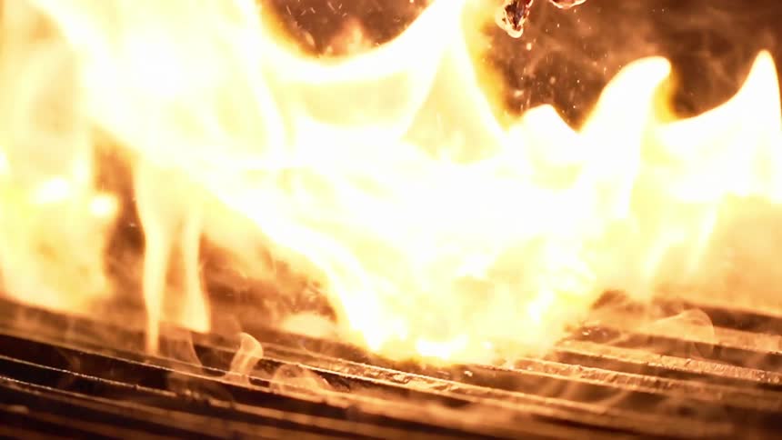 A slab of grilled steak is being flipped over on an open flame grill