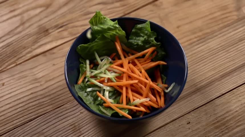 Sliced vegetables in a salad inside a blue ceramic bowl over a wooden table