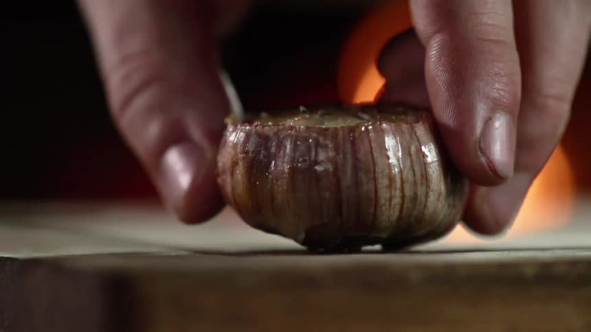 A white man sets an onion down on a wooden plank
