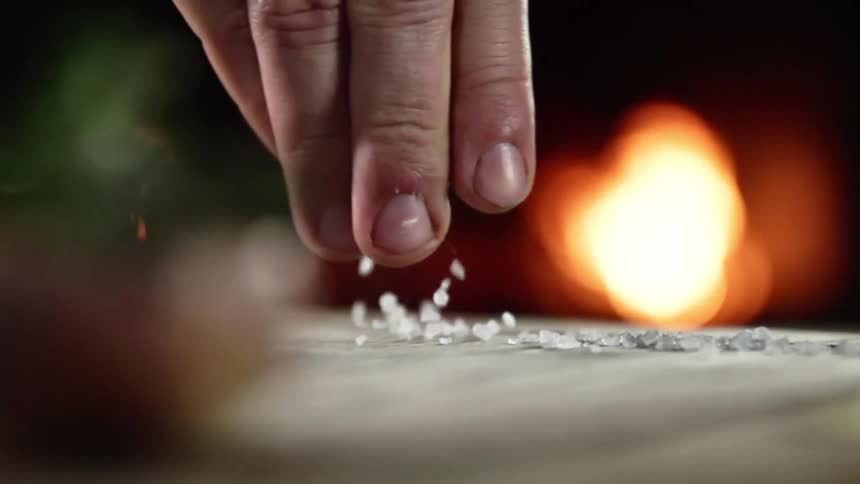 A white man sprinkles large grains of salt on a table