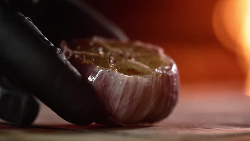 Roasted garlic is placed on a surface by a gloved hand