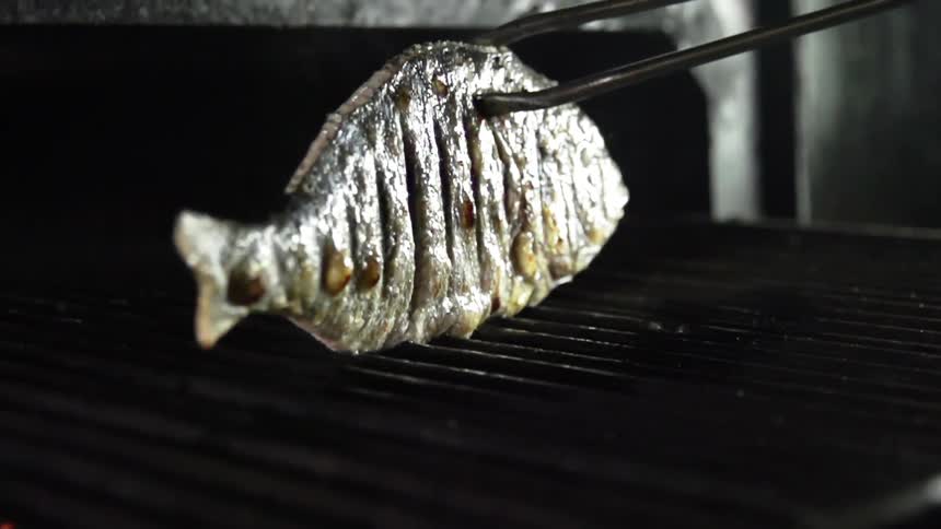 Tongs flip a whole fish cooking on an indoor grill