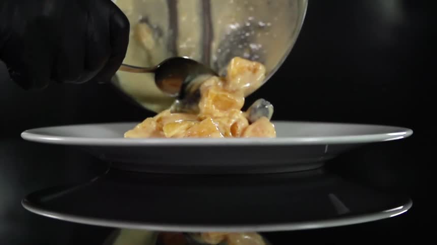 Person wearing black gloves scoops entree onto plate sitting on reflective surface using spoon