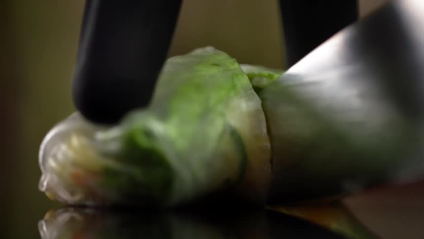 A gloved person holds a piece of food as a knife cuts through it
