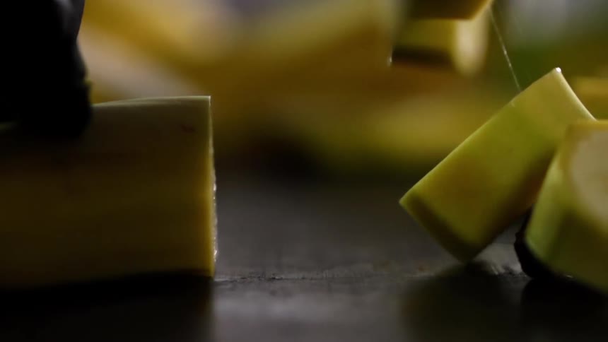 Chef wearing black latex gloves chops a whole banana with a sharp kitchen knife