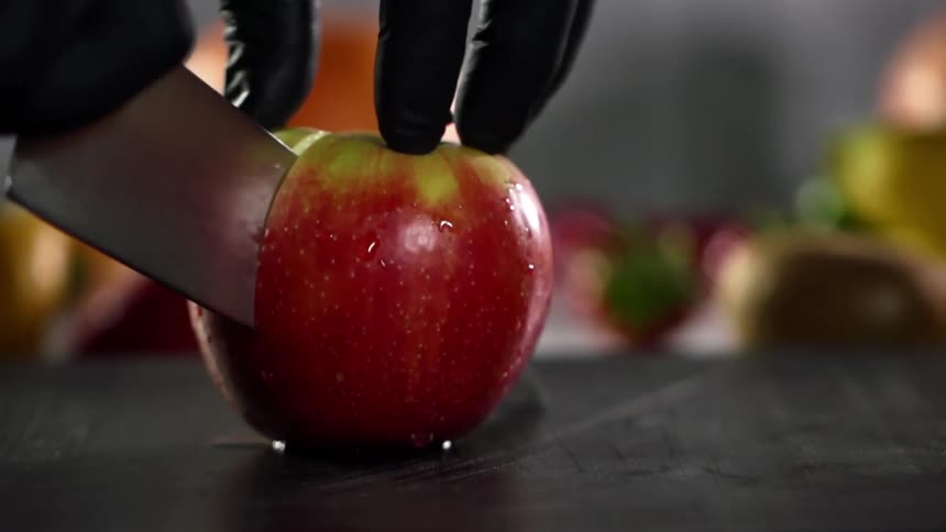 Close up of hands wearing black gloves cutting a red apple in half