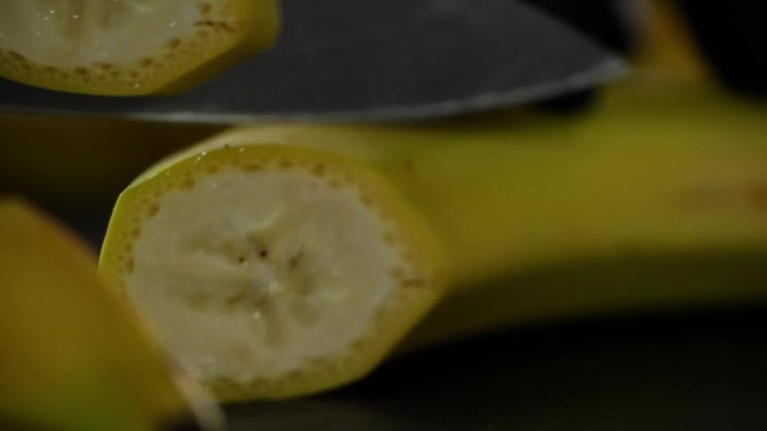 Close up of a knife cutting a curved banana with yellow skin