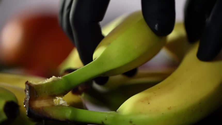 Close up of hands wearing black gloves taking a banana from a bunch of bananas