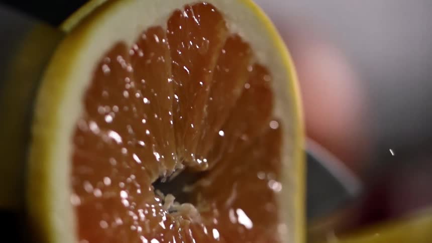 Juice flying out of a grapefruit as a knife cuts in to it