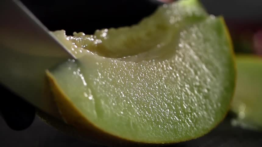 Cook with black gloves slices a melon with a knife