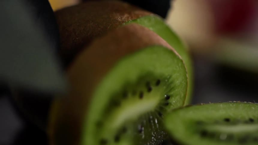 A person cuts a kiwi with a kitchen knife
