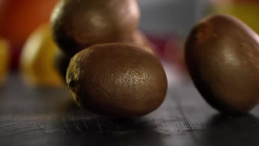 Close up of kiwis with brown skin covered in hairs falling on the countertop