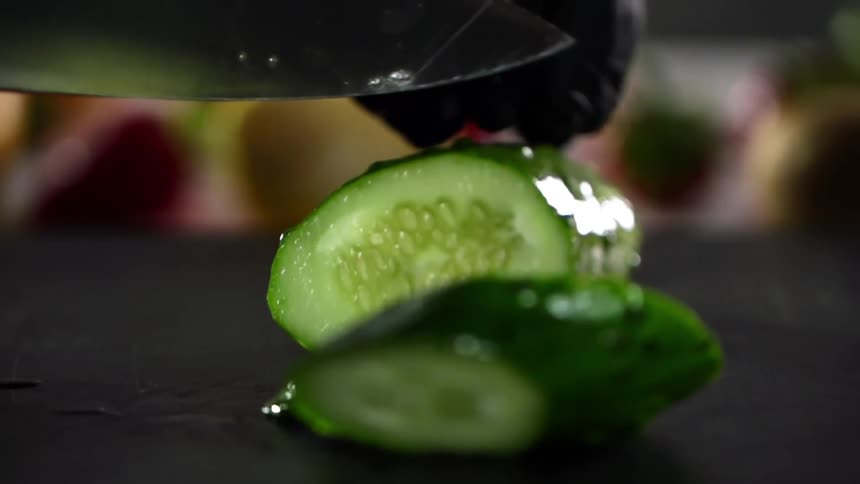 Gloved hands slice a cucumber with a knife