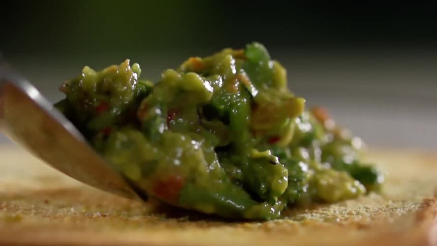 A spoonful of avocado is placed onto toast