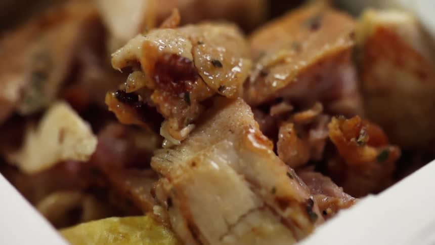 Chopped pieces of fried pork belly falling into a cardboard takeout box