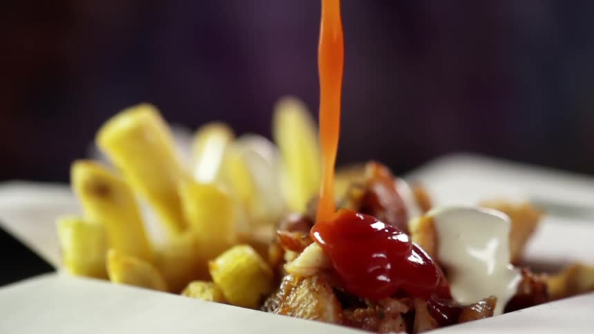 A large amount of ketchup is added to a takeout container of chicken and fries
