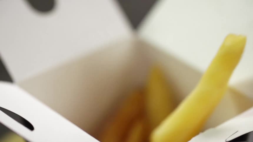 An open takeout box is being filled by having french fries poured into it