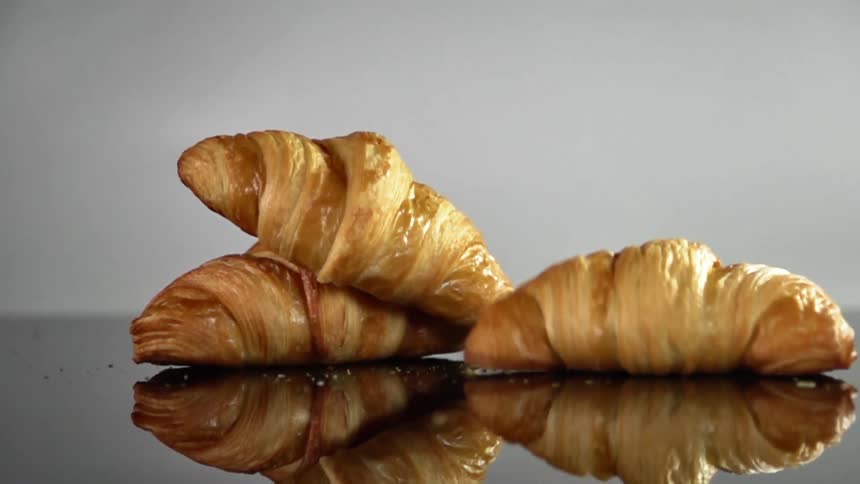 Three croissants drop onto a reflective table