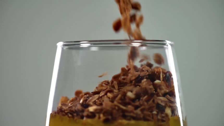 Granola with raisins falling into a glass cup filled with orange juice