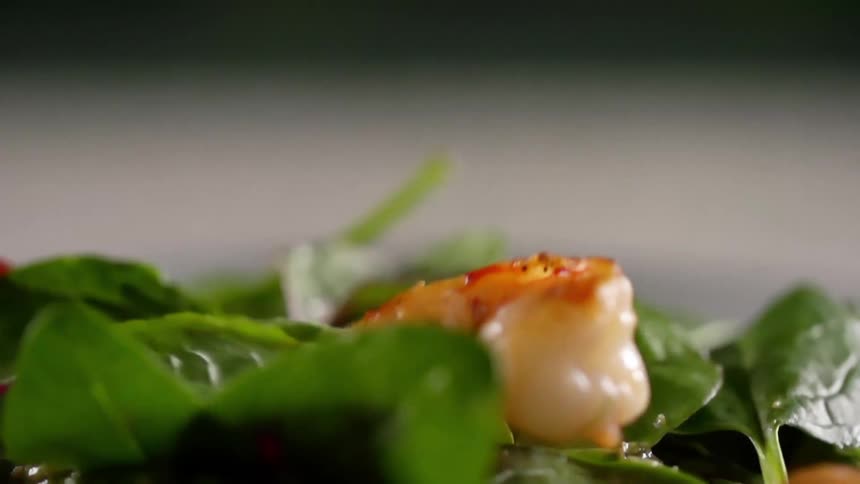 A couple of pieces of shrimp are dropped onto a pile of spinach leafs