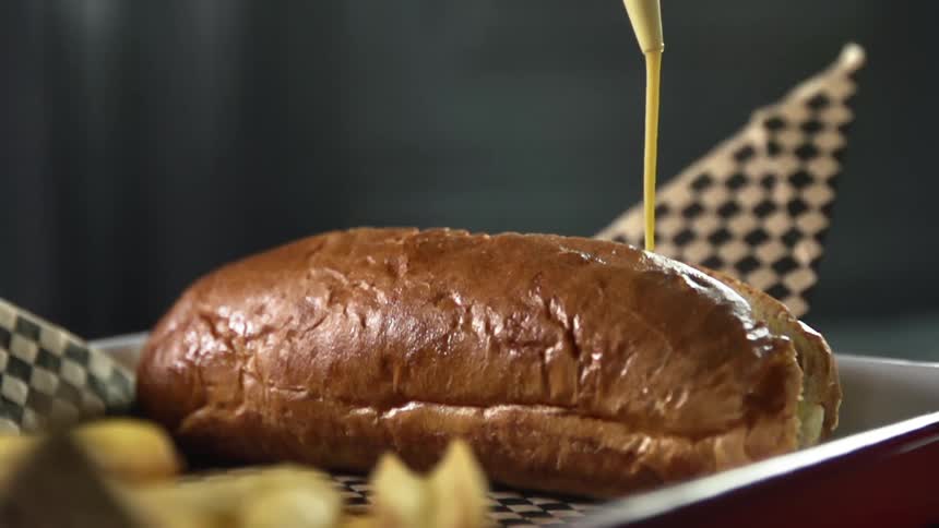 Mustard is being poured on the bun