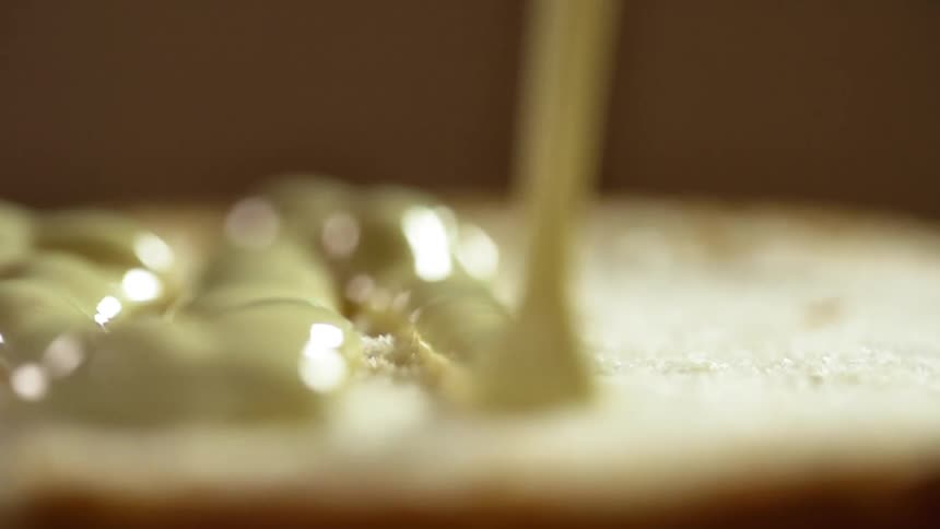 Bottom half of a hamburger bun being poured with mayonnaise