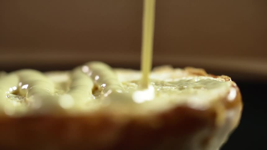 A sliced burger bun has mayo slowly poured over its cut surface