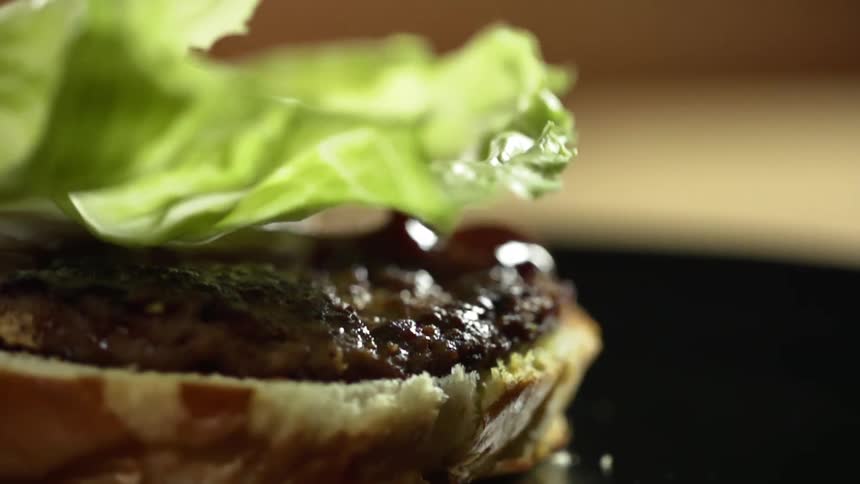 A piece of lettuce drops on a hamburger patty