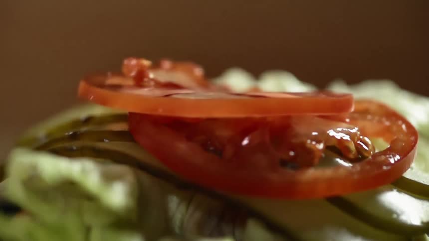 Two slices of tomato are dropped onto a small stack of sliced pickle spears