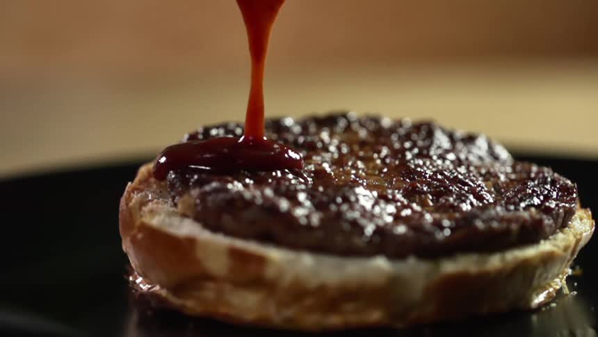 Ketchup pouring over a burger patty sitting on a bun
