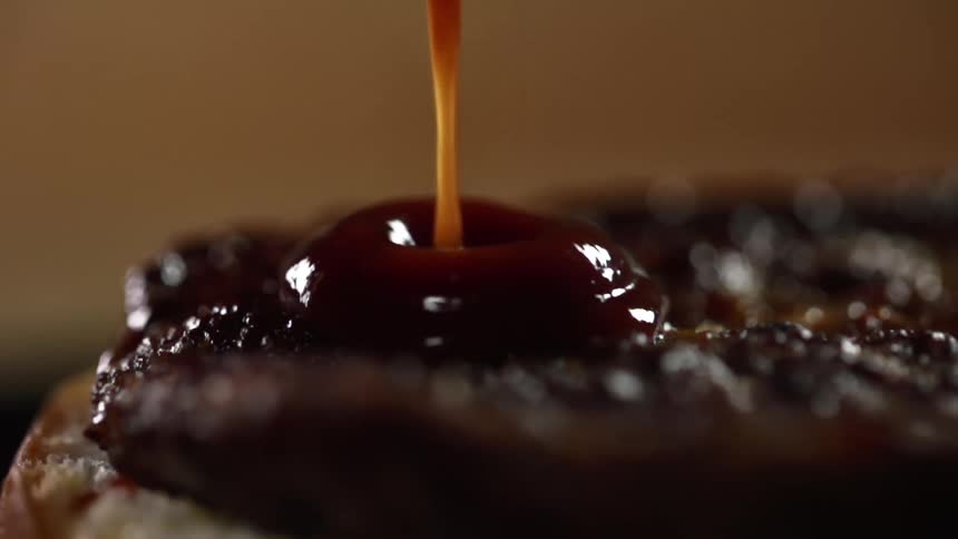 Barbecue sauce pours onto a burger patty