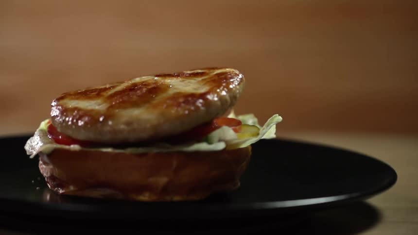 A chicken patty falls on a bun with lettuce and tomatoes on it