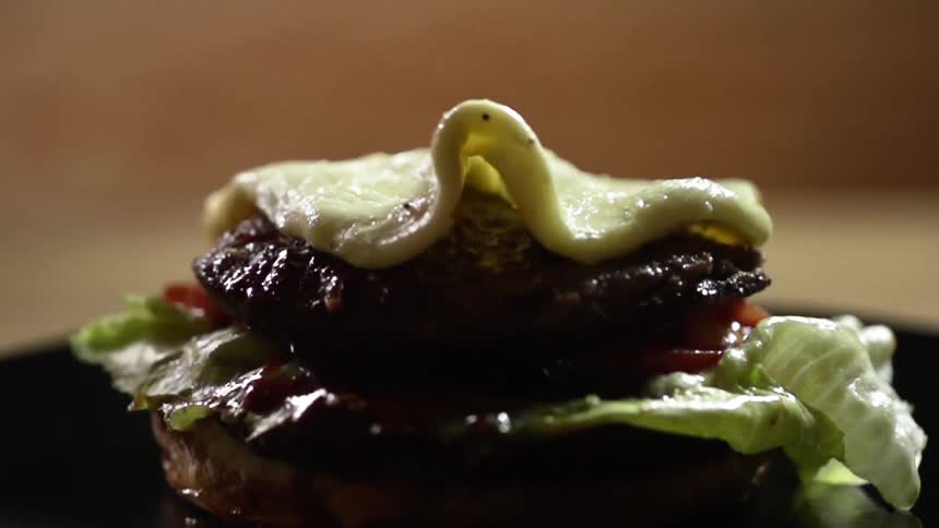 A fried egg drops down onto a hamburger patty on a  bun with lettuce and tomatoes