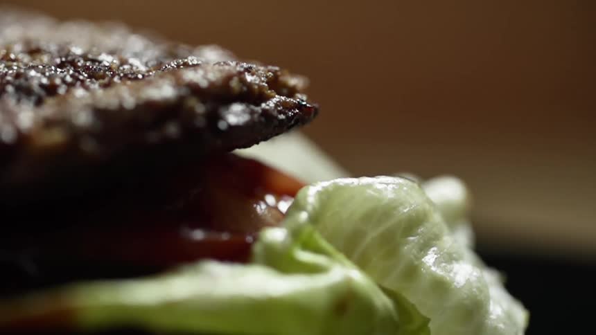 A burger patty falls on a pile of lettuce and tomatoes