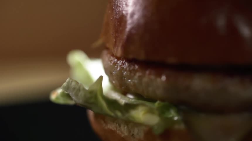 A bun top is dropped on a hamburger patty