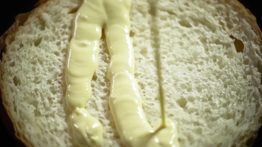 Bottom half of a hamburger bun being poured with mayonnaise