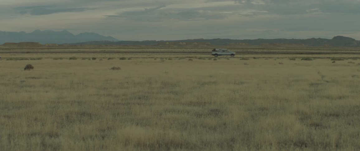 Trucks and cars are driving on a road through a prairie on a cloudy day