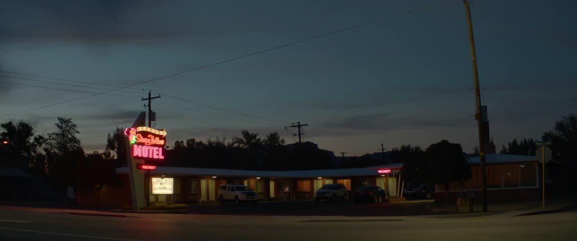 The neon lights on a motel sign are glowing and flashing at dusk